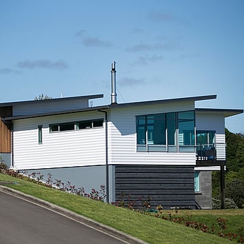 Modern home clad with white timber and situated on sloping hill. 