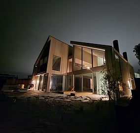 Night-time exterior of bespoke beachfront home on Ocean Beach Road with warm cedar cladding, high ceilings and floor-to-ceiling glazing by MB Construction.