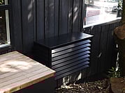 Black Wall hung heatpump cover on bush house. Blending in.