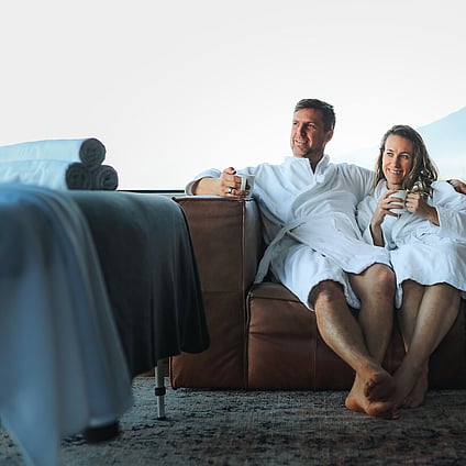 A couple relaxing on a couch in robes ready for their Indulge Mobile Spa treatment.