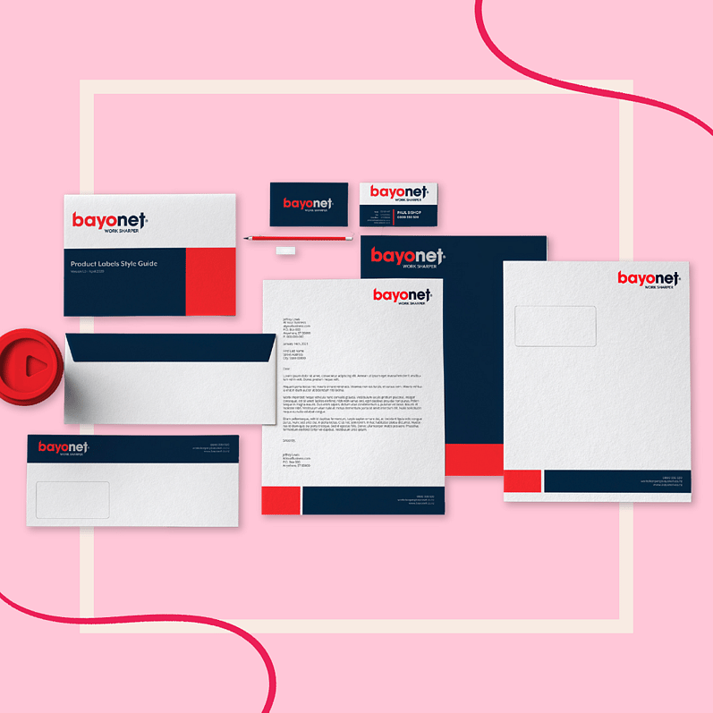 Bayonet branded stationery including a product label style guide, business cards, envelopes, letterhead, pen, and a seal, arranged on a pink background