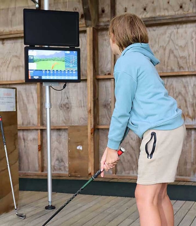Boy looking at Toptracer screen in driving range getting ready to hit