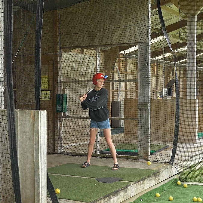 Woman standing in baseball batting cage with red helmet