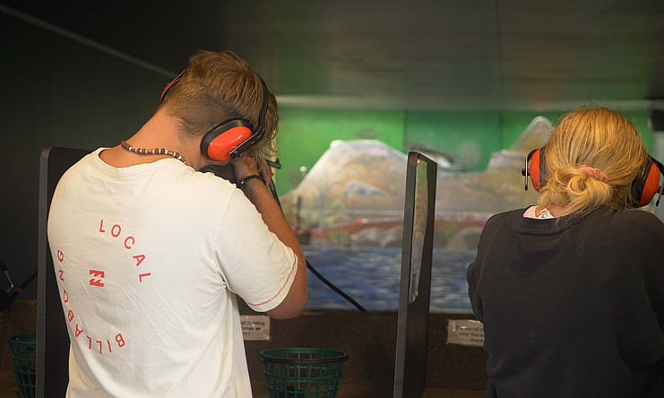 Young man and woman shooting at air rifle range pointing at targets