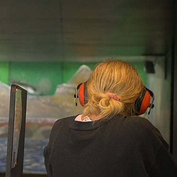 Woman facing toward indoor shooting range and aiming air rifle