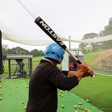 Man in baseball batting cage with blue helmet and auto pitching machine
