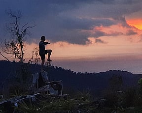 Person balancing on one leg with pink sunset in background
