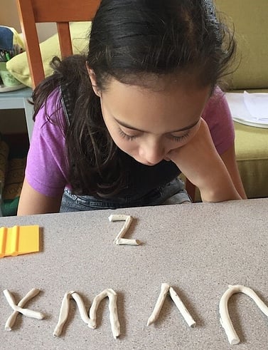 Young girl sitting at table with clay alphabet