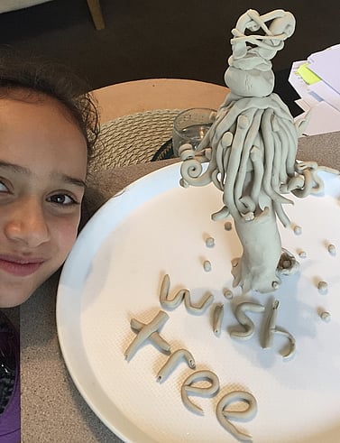 Young girl smiling beside her clay wish tree