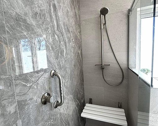 Accessible shower with stylish tiles, built-in seat, and stainless steel grab rail for safety