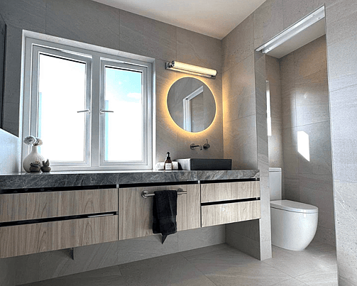 Bathroom renovation featuring a modern vanity with a round mirror light and a separate toilet visible in the background