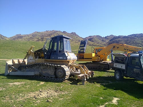 On-site hydraulic repairs by Andy's Engineering & Mechanics (AEM) to D12 bulldozer and digger against a clear blue sky.