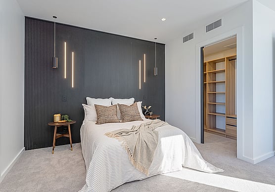 Modern bedroom with bed, feature wall, lighting and a walk-in-closet.