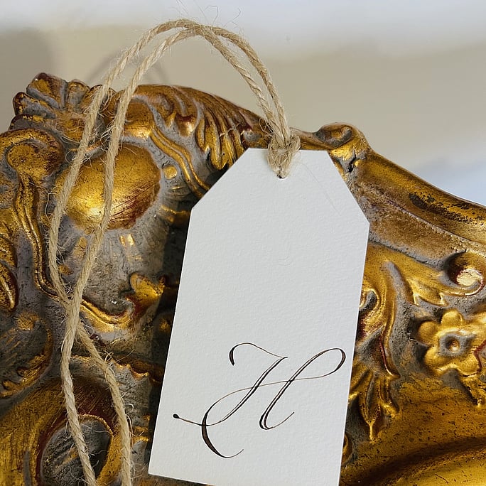 An alphabetic H gift tag displayed on a gold ornate mirron