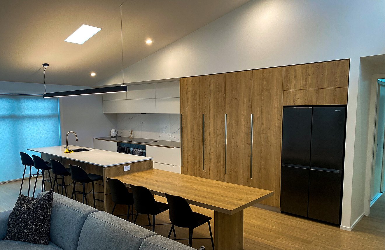 Hero image of a sleek modern kitchen with integrated appliances, large island, and custom joinery by Barrett Joinery in Timaru.