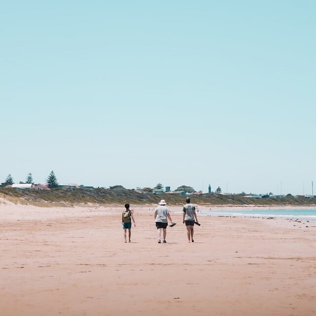 Three people walking down a beach together.