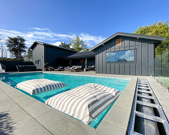 A view from a pool looking onto a black barn with pool pavillion