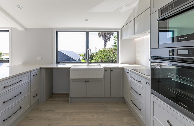 A newly completed kitchen renovation in Papamoa. A grey country-styled kitchen and wood-look laminate flooring. The kitchen has a new ceiling and new joinery. The large kitchen window looks out onto the ocean view at Papamoa Beach.