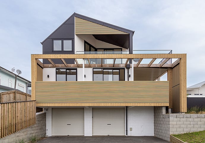 A newly renovated beach bach completed by renovation builders in Papamoa. Shows a three-story home with twin garages on the lower level, and on the second and third levels, the living areas with large windows, new joinery, and expansive decks on both levels.