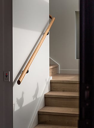 A close up image of a new stair case with timber handrail and stairs encapsulated with laminate flooring.