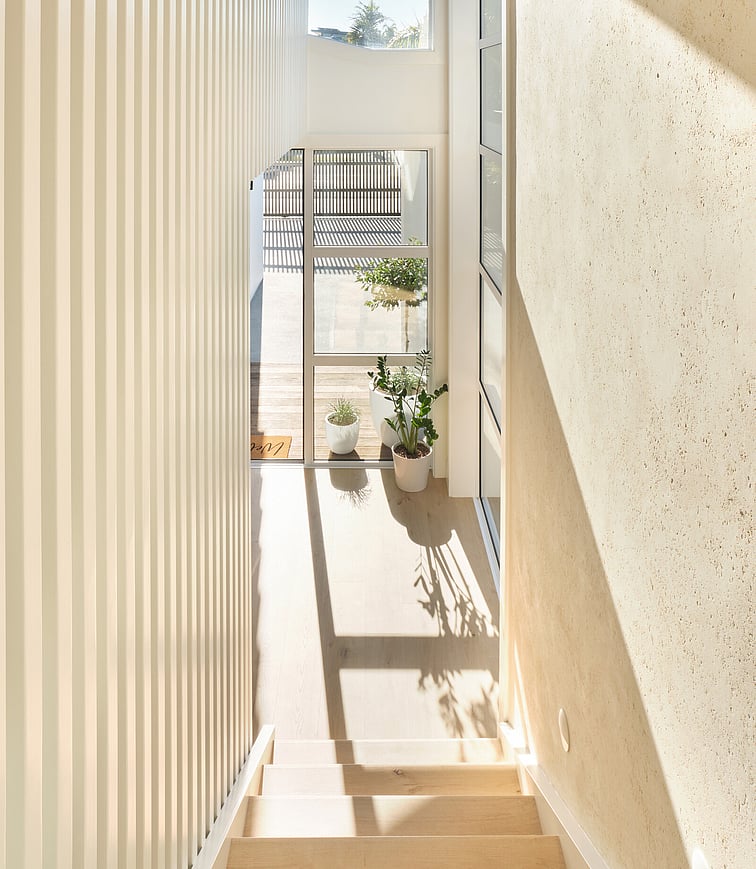 An outdoor kitchen at night with warm lighting illuminating the space. The outdoor kitchen sits on hardwood decking and shows a wooden table, pizza oven, and kitchen units. The area is covered by a beautiful raked ceiling.