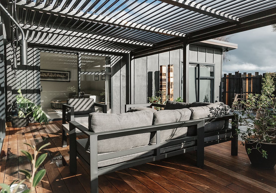 New deck, home, and pergola in black. Outdoor furniture has been placed on the new deck. The pergola louvres are open to let sunlight in.  