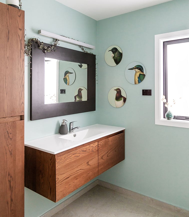 An outdoor kitchen at night with warm lighting illuminating the space. The outdoor kitchen sits on hardwood decking and shows a wooden table, pizza oven, and kitchen units. The area is covered by a beautiful raked ceiling.