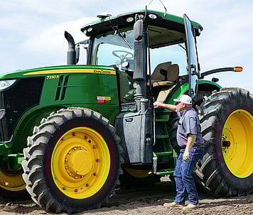 Farmer inside a John Deere tractor using Trimble auto-steering for hands-free operation.