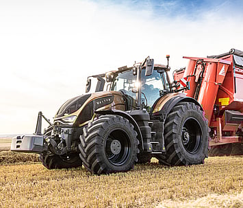 Valtra S Series tractor operating in a field, hitched to a red trailer, demonstrating its high horsepower capabilities in an agricultural setting.