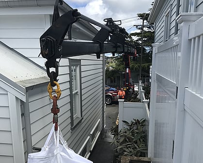 Photo of a hiab crane arm carefully moving item between two houses
