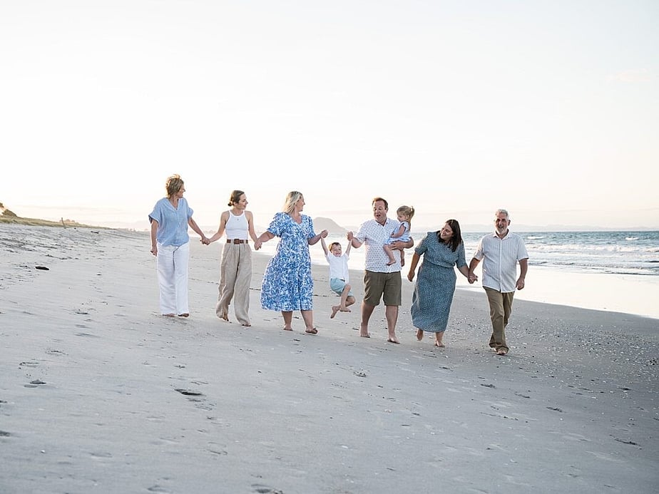 Family on the beach in blue and white clothing swinging boy by the arms having fun during Family Photoshoot