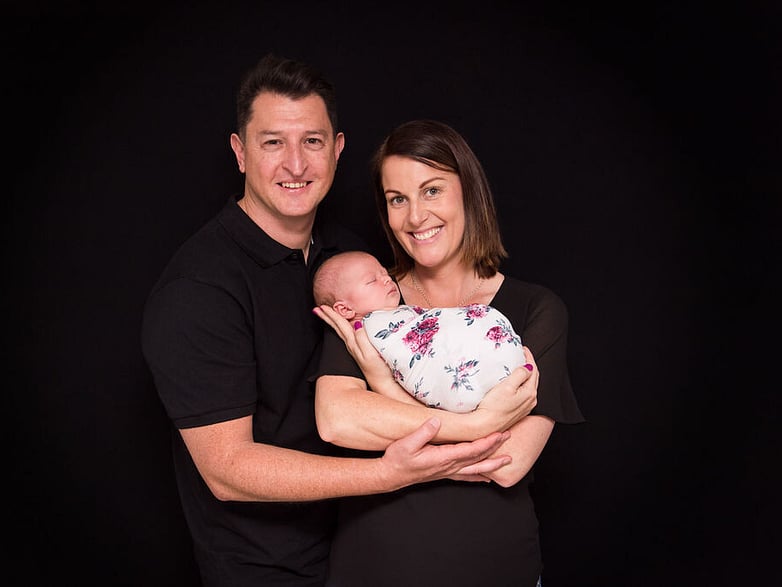 Mum and Dad holding newborn baby girl on a black backdrop