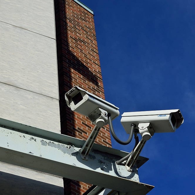 A photo showing 2CCTV cameras installed on metal framework on the side of a commercial brick and stone building.