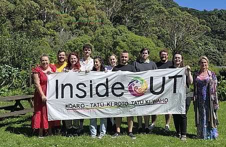 Group of people outdoors holding InsideOUT banner with trees and greenery in background during community event