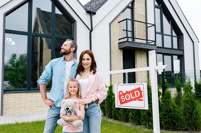 family outside their home with a for sale sign