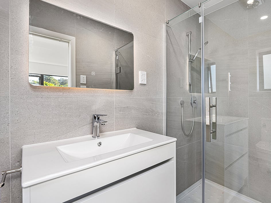 Bathroom with stony coloured tiles and white basin in Eden Construction&rsquo;s new build house on Mountain Road, Mangere Bridge, Auckland.