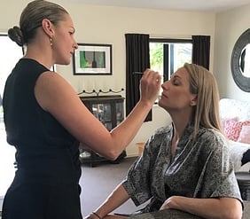 Krystal standing in front of a seated woman to whom she is applying makeup