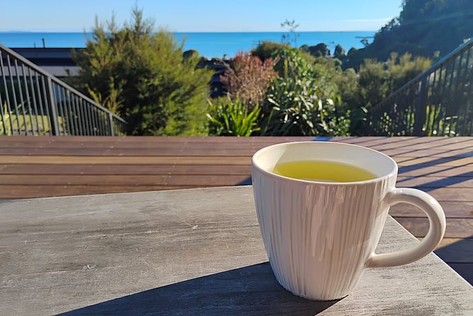A mug of green tea on a table with a New Zealand sea view in the background
