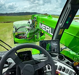 Telehandler cab looking at the boom with a bale grab carrying a hay bale.