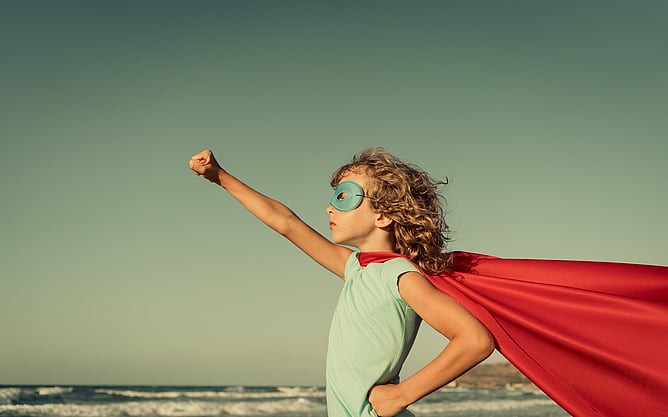 Child in front of the ocean wearing a red superhero cape and mask